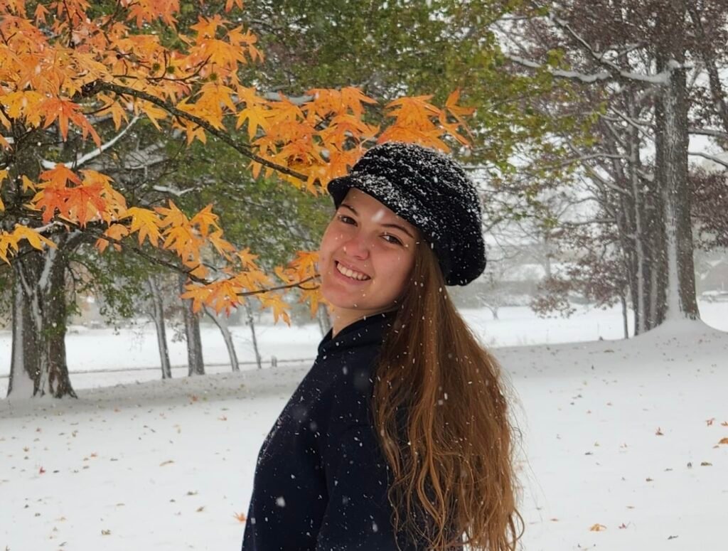 Rachel smiling with fall colors behind her and snow falling.